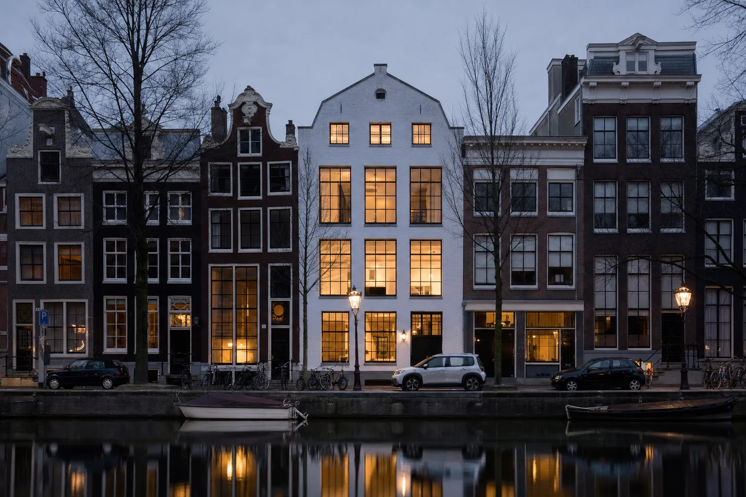 A white-brick house on an Amsterdam canal at blue hour, its tall windows lit